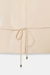 Camisa de manga larga color beige claro, con cuello solapa, escote pico y detalle de cinturón fino a tono que se anuda en la cintura.