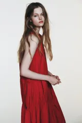 Vestido midi de color rojo confeccionado en tejido de nylon. Presenta un diseño sin mangas con cuello redondo y detalles de frunces horizontales con lazadas laterales ajustables. Cuenta con un cierre en la espalda mediante abertura y botón.