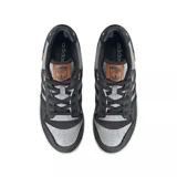 Championes adidas modelo Rivalry Low, con diseño de corte bajo. Presentan una combinación de paneles en cuero gris y denim oscuro con bordes deshilachados. Incluyen las icónicas tres tiras laterales en negro, suela de goma color crema y detalles en cuero marrón en la lengüeta y el lateral.