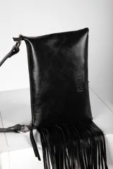 Cartera bandolera de cuero negro con flecos colgantes en el lateral, cierre superior y correa ajustable con argollas metálicas.