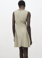 Vestido corto verde militar con cuello barco, sin mangas y diseño recto. Presenta detalles de pliegues en los laterales y cierre de cremallera en la parte posterior.