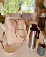 Bolso matero color beige con textura croco, con correa larga regulable y bolsillo exterior para lentes.