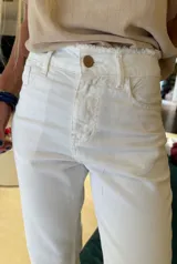 Jean de mezclilla color blanco roto (off-white) de corte recto, con detalle desflecado en el borde de la cintura y en los tobillos. Presenta costuras claras y botón metálico en el cierre.