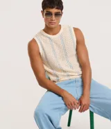 Musculosa de punto para hombre en color beige con rayas verticales finas en color celeste. Presenta un diseño con textura perforada, cuello redondo y terminaciones acanaladas en cuello, sisas y ruedo. Confeccionada en 100% algodón.