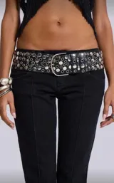 Cinto negro de cuero sintético con diseño de múltiples tachas metálicas circulares y hebilla plateada.