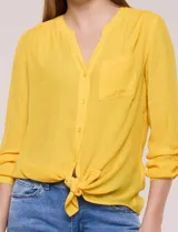 Blusa de calce relajado color salmón, confeccionada en tela liviana con textura sutil. Presenta escote en V con abotonadura frontal, bolsillo parche en el pecho, mangas largas regulables con presilla y ruedo con opción de anudar en el frente.