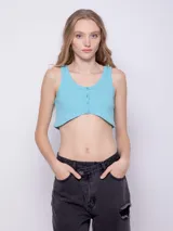 Top blanco de tela texturada, sin mangas y con cuello redondo. Cuenta con cuatro botones y terminación en curva en la parte delantera.