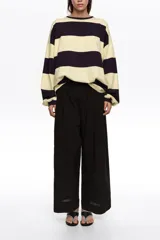 Pantalón tobillero de corte campana color negro, confeccionado en mezcla de algodón y viscosa. Presenta cierre frontal con botón, tiro medio, bolsillos diagonales, cinturilla elástica y vuelta en el bajo de la pierna.
