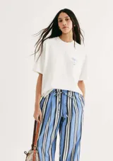 Remera blanca de manga corta, corte oversized, cuello redondo y pequeño estampado azul en el pecho con diseño de palmera y texto.