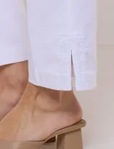 Pantalón ankle de tiro alto color blanco, confeccionado en tejido elástico con pretina ancha tipo pull-on, corte entallado y detalle de encaje calado en las aberturas laterales del ruedo.