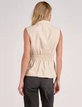 Chaleco entallado color beige, con cuello solapa tipo sastre, escote en V y cierre frontal con botones en contraste. Presenta cintura elastizada que define la silueta con un ligero vuelo en el ruedo.