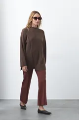 Polera de tejido de punto color marrón, con diseño asimétrico y costura diagonal frontal. Presenta cuello alto, hombros caídos, mangas largas con puños acanalados y ruedo con abertura frontal.