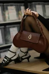 Cartera tipo baguette de cuero nobuk color musgo con detalles en cuero marrón. Tiene correa al hombro regulable, cierre YKK de aluminio plateado, chapa de marca central y logo grabado en la parte trasera.