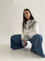 Cardigan de punto con diseño jacquard de inspiración nórdica, en tonos blanco, gris y marrón. Presenta cuello redondo, cierre frontal con botones y mangas largas con puños acanalados.