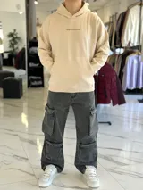 Canguro oversize de color beige con capucha y bolsillo tipo canguro al frente. En la espalda cuenta con un gran estampado tipográfico en marrón con la frase "Own Your Story", texto descriptivo y un logotipo ovalado con las letras "EST 2021".