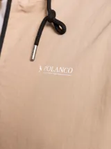 Campera de nylon con capucha, cierre frontal y forro de red. Presenta un diseño minimalista en color beige con detalles en negro.