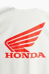 Remera de algodón color blanco con cuello redondo y estampado frontal con el logo de Honda en color rojo.