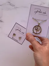 Conjunto de joyería compuesto por un collar con dije circular de libélula y un par de aros tipo caravana con diseño de libélula pequeña, ambos en acero quirúrgico.