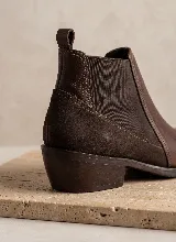 Bota tipo Chelsea de cuero negro con paneles laterales elásticos y taco bajo cuadrado. Presenta una combinación de texturas en el cuero y una presilla trasera para facilitar el calce.