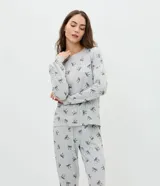 Pijama de dos piezas confeccionado en tejido de punto, compuesto por una blusa de manga larga con cuello redondo y puños ajustados, y un pantalón recto con cintura elástica. Presenta un estampado continuo de moñitas sobre fondo gris.