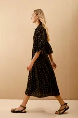 Vestido midi negro con lunares dorados, escote en V, mangas anchas al codo con bordado de lentejuelas y mostacillas. Corte amplio con ajuste elástico en la cintura y forro de algodón.