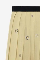Falda de tiro medio confeccionada en hilatura de lino, color beige con bloques negros y detalles de abalorios y ojales metálicos aplicados a contraste. Cuenta con cierre lateral con cremallera oculta en costura.