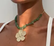 Collar con cadena de piedras irregulares en color verde y un dije central grande en forma de flor dorada con textura grabada.