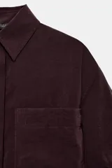 Camisa de manga corta con cuello solapa, confeccionada en tejido fluido con acabado satinado. Presenta un bolsillo frontal, cierre con botones ocultos y mangas con dobladillo.