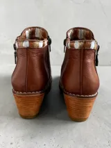 Botas cortas de cuero en tonos marrón y tostado, con paneles de cuero vacuno con estampado animal print tipo ponchada y detalles pintados a mano en dorado. Presentan punta fina, taco cuadrado de madera, costuras visibles a contratono y doble cierre lateral con tiradores metálicos personalizados.