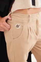 Pantalón recto de tiro medio confeccionado en pana con lycra. Presenta pinzas frontales, bolsillos laterales y traseros, y cierre con botón dorado. El diseño destaca por el detalle de paño espigado en el interior del ruedo, visible al doblarlo, y un pin bordado decorativo en el bolsillo delantero.
