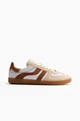 Calzado deportivo con exterior tejido blanco y detalles en gamuza marrón y beige, con cordones frontales y suela de goma.