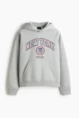 Canguro H&M de mezcla de algodón en color gris melange, con capucha de doble capa, bolsillo tipo canguro y hombros caídos. Presenta un estampado frontal con la inscripción "NEW YORK PHYS. ED." en tonos azules y rojos con detalles de escudo.