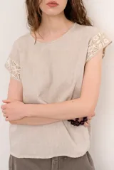 Blusa de lino color blanco con detalles de crochet en tono verde militar en los hombros, cuello redondo y manga corta.