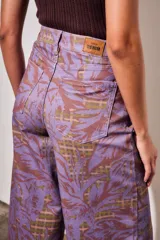 Pantalón jean de tiro alto y corte wide leg, con estampado de hojas grandes en tonos morados y fondo con patrón a cuadros.