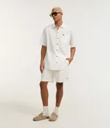 Camisa de corte relajado para hombre, confeccionada en una mezcla de cáñamo y algodón. Presenta cuello inglés, mangas cortas, cierre frontal con botones y un bolsillo de parche en el pecho con una pequeña etiqueta de la marca Ripping.