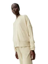 Chaqueta deportiva color beige claro, estilo bomber, con cierre frontal y cuello redondo. Presenta mangas murciélago y un calce holgado.