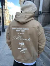 Canguro tostado de algodón con capucha, puños y cintura acanalados. Estampado en la espalda con la frase "East London Studios Since 1994", el logo de Allsaints y nombres de ciudades.