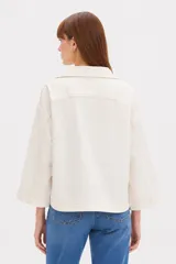 Sobrecamisa de lino y viscosa color marfil, con cuello solapa, mangas tres cuartos anchas, bolsillos frontales con solapa y cierre de botones oscuros.