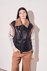 Chaleco negro de cuero sintético con interior de piel sintética color beige, cierre frontal con cremallera y corte oversize.