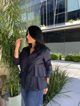 Camisa azul marino de manga larga con cuello camisero y cierre de botones. Presenta volantes horizontales en la parte delantera.