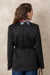 Chaquetón color beige de corte recto y largo, con cierre frontal mediante botones y lazo ajustable en la cintura. Presenta cuello en V, bolsillos laterales con solapa y mangas largas.