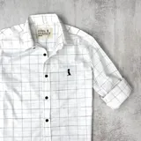 Camisa de manga larga de algodón color blanco con diseño a cuadros finos en negro, cuello italiano, cierre con botones marrones y logo bordado en el pecho.