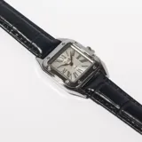 Reloj de pulsera con caja cuadrada plateada y correa de cuero negra con textura.