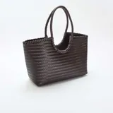 Bolso de mano grande con diseño rectangular y textura trenzada en color marrón oscuro. Cuenta con dos asas circulares trenzadas integradas en la estructura.