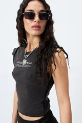 Remera sin mangas, ajustada al cuerpo, color gris oscuro o negro gastado, con cuello redondo y terminaciones de volados en las sisas. Estampado frontal con texto en blanco que dice "*rea ess*" y "*fearless*".