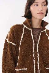 Campera de tejido de punto color marrón con destellos de lurex, corte oversize y cierre frontal. Presenta detalles de costuras y terminaciones en color crema, cuello alto y bolsillos frontales.