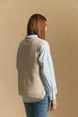 Chaleco tejido color azul, con escote en V, cierre frontal con botones y diseño de líneas verticales en relieve. Presenta terminaciones acanaladas en el ruedo y un borde ondulado en el escote.