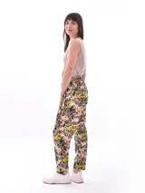 Pantalón babucha de tiro alto con cintura fruncida y lazo para ajustar. Estampado de hojas tropicales en tonos naranja y marrón sobre fondo blanco.