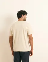 Remera básica de algodón color beige, de manga corta, con cuello redondo y un pequeño detalle bordado en el pecho.