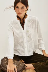 Camisa blanca de manga larga con cuello mao y escote en V. Presenta bordados florales en blanco y dorado en el frente.